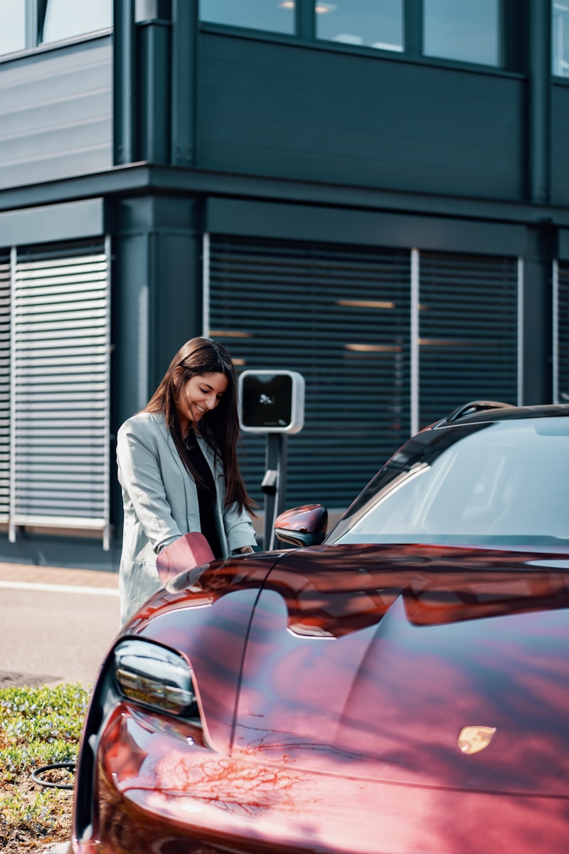 Photo by JUICE a woman standing next to a red car